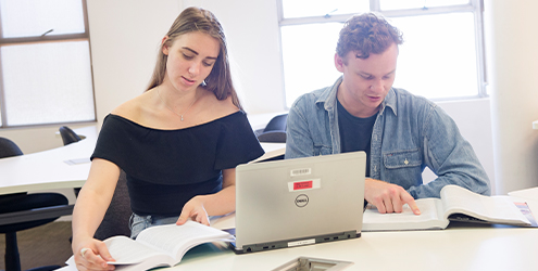 Female and male students revising books and laptop notes together