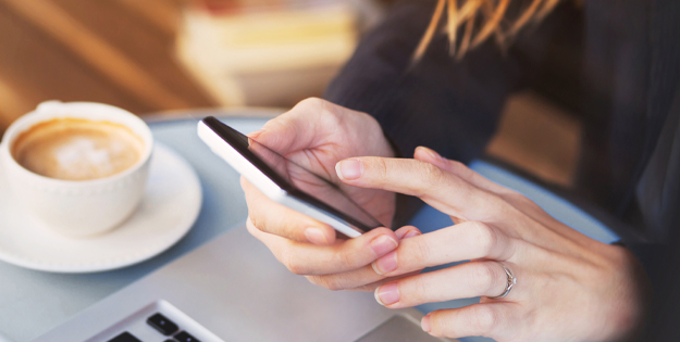 A lady sitting at a table drinking coffee and managing her finances on a phone app