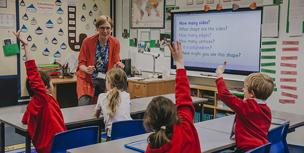 Children raising hands in primary school classroom