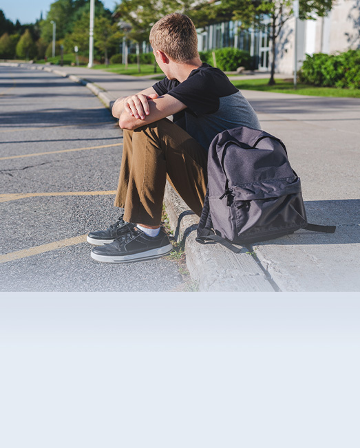 A teenage boy alone and waiting on a roadside curb.