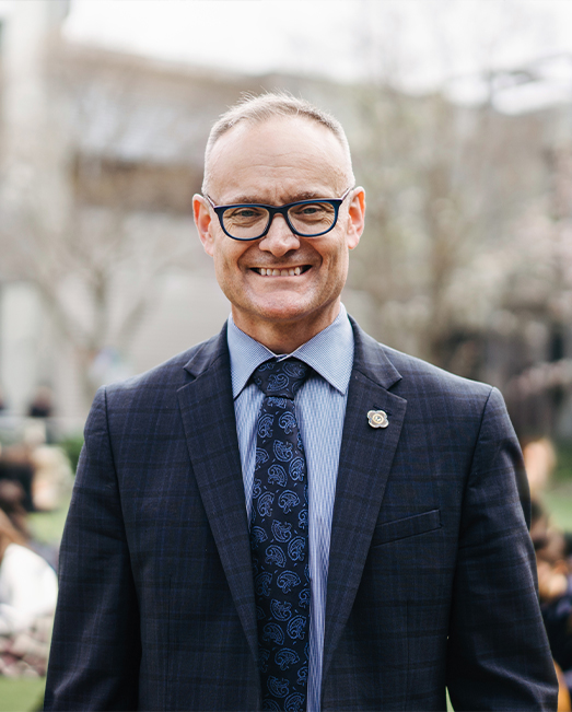 Brendan Watson smiling to camera with his school campus in the background
