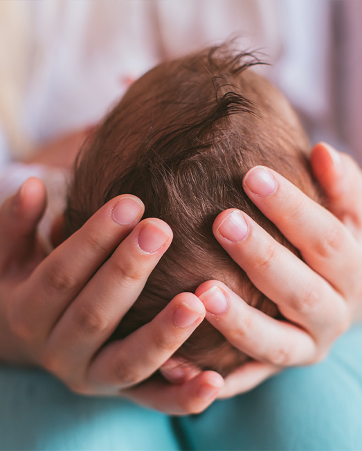 The top of a baby's head cradled by female hands