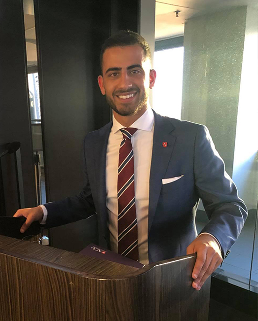 George Mourani standing behind a lectern smiling at camera
