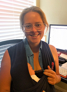 Dr Kristie Flannery cradling newborn while she works at a computer